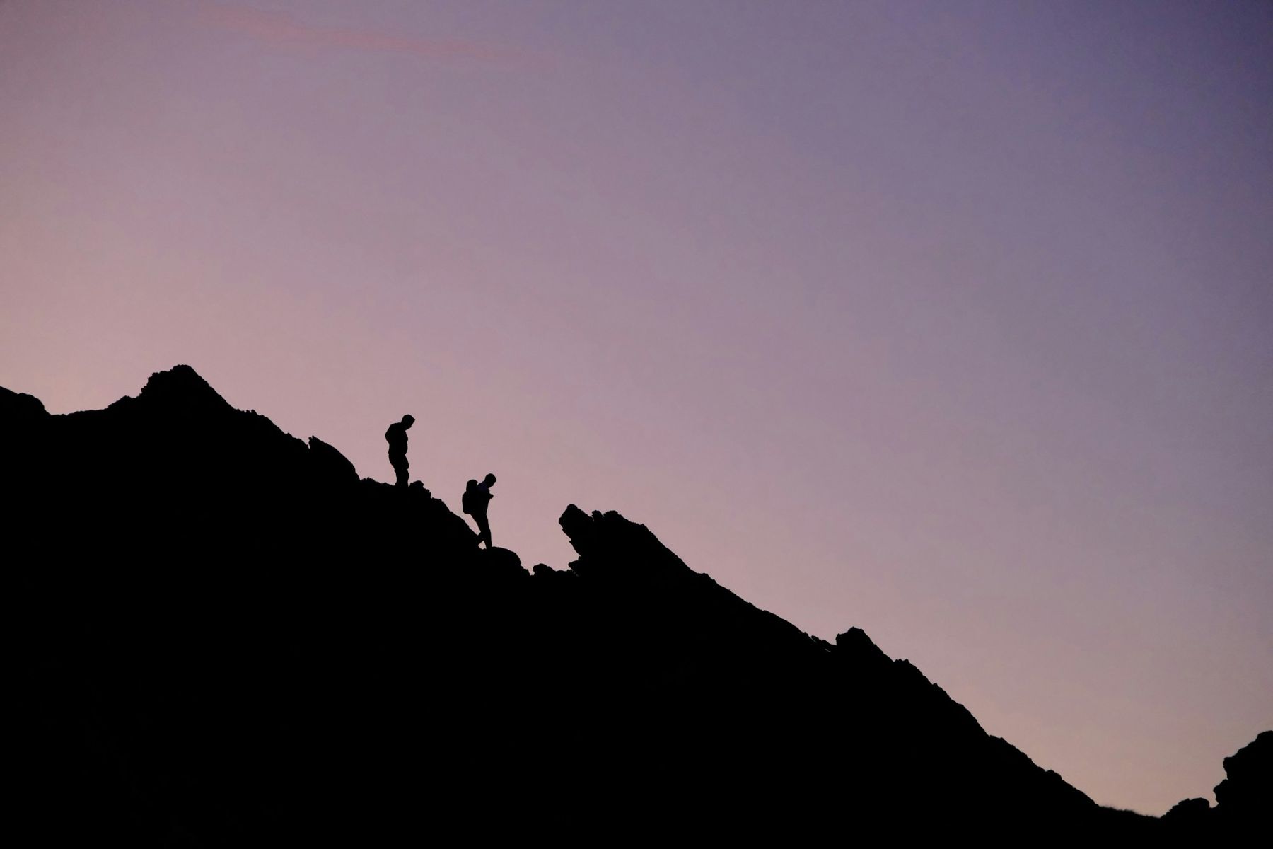 Two silhouetted climbers descending a ridge at dusk